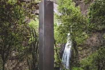 Estructura en cuatro lados, cada uno escrito en hebreo, chino mandarín, alfabeto árabe, y ruso. Monolito misterioso con cascada natural y perro feliz.